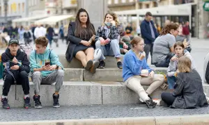 Grupa młodych ludzi siedzi na schodach, każdy zajęty telefonem. Czy to ich sposób na "flex"?