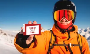 Narciarz w kasku i goglach pokazuje kartę "Snow Card Tirol". To jest skipass, który umożliwia dostęp do wyciągów.