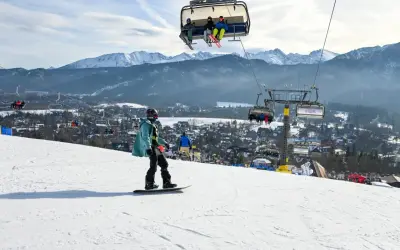 Snowboardzista na stoku, w tle kolejka krzesełkowa i góry. Zastanawiasz się, ile kosztuje karnet na narty?