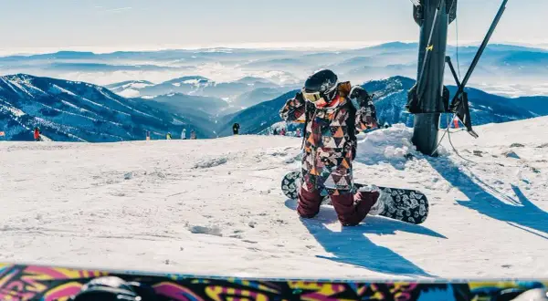 Dziecko w kolorowym kombinezonie przygotowuje się do zjazdu na snowboardzie. Idealne miejsce, gdzie na narty w Czechach z dziećmi.
