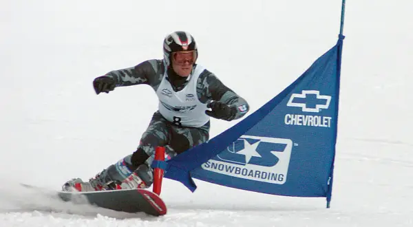 Snowboardzista w kasku i goglach mija niebieską flagę z logo Chevrolet. To sport, który zyskał popularność w XX wieku, choć jego korzenie sięgają wcześniejszych lat.