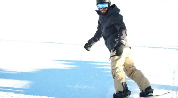 Mężczyzna w kasku i goglach zjeżdża na snowboardzie. Zastanawiasz się, ile kosztuje wypożyczenie snowboardu?